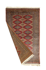 Alfombra doblada mostrando el reverso y el anverso, revelando el intrincado diseño simétrico en tonos tierra y rojo.