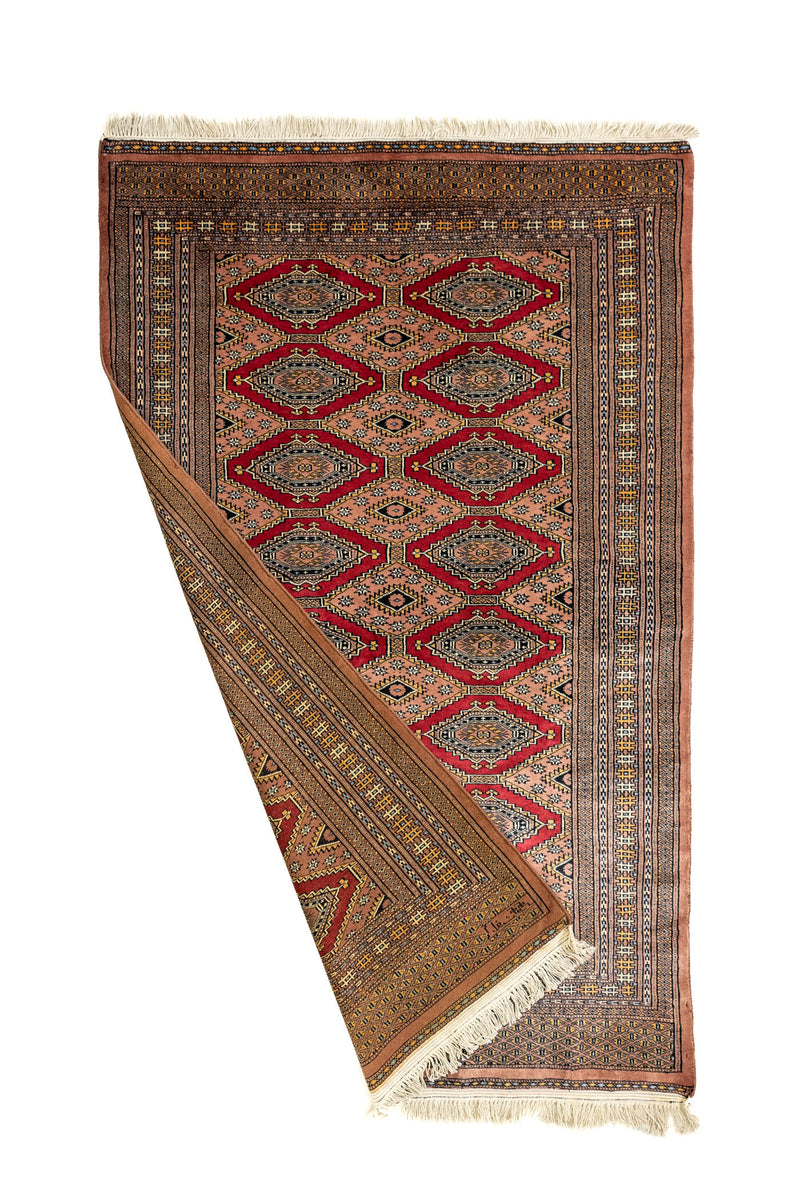 Alfombra doblada mostrando el reverso y el anverso, revelando el intrincado diseño simétrico en tonos tierra y rojo.