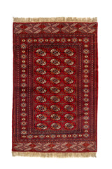 Vista completa desde arriba de una alfombra oriental roja con patrones repetitivos tipo "gul" en marfil y negro, y guardas decoradas con rombos.