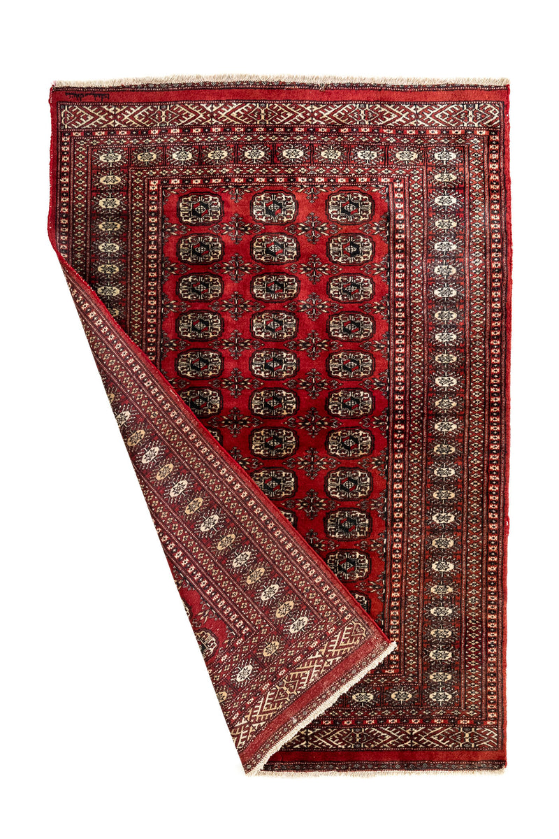 Imagen de la alfombra parcialmente doblada, mostrando el reverso tejido y el borde decorado con motivos geométricos.