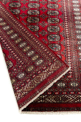 Primer plano del borde y reverso de la alfombra oriental, destacando la calidad del tejido y los motivos geométricos.