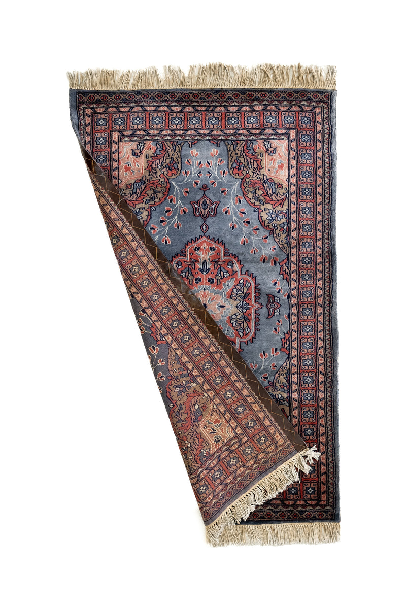 Alfombra con una esquina doblada revelando el reverso tejido y los flecos largos, mostrando la calidad artesanal del acabado.