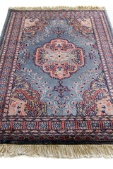 Imagen en perspectiva de la alfombra, resaltando el medallón central simétrico y el fondo gris con motivos florales estilizados.