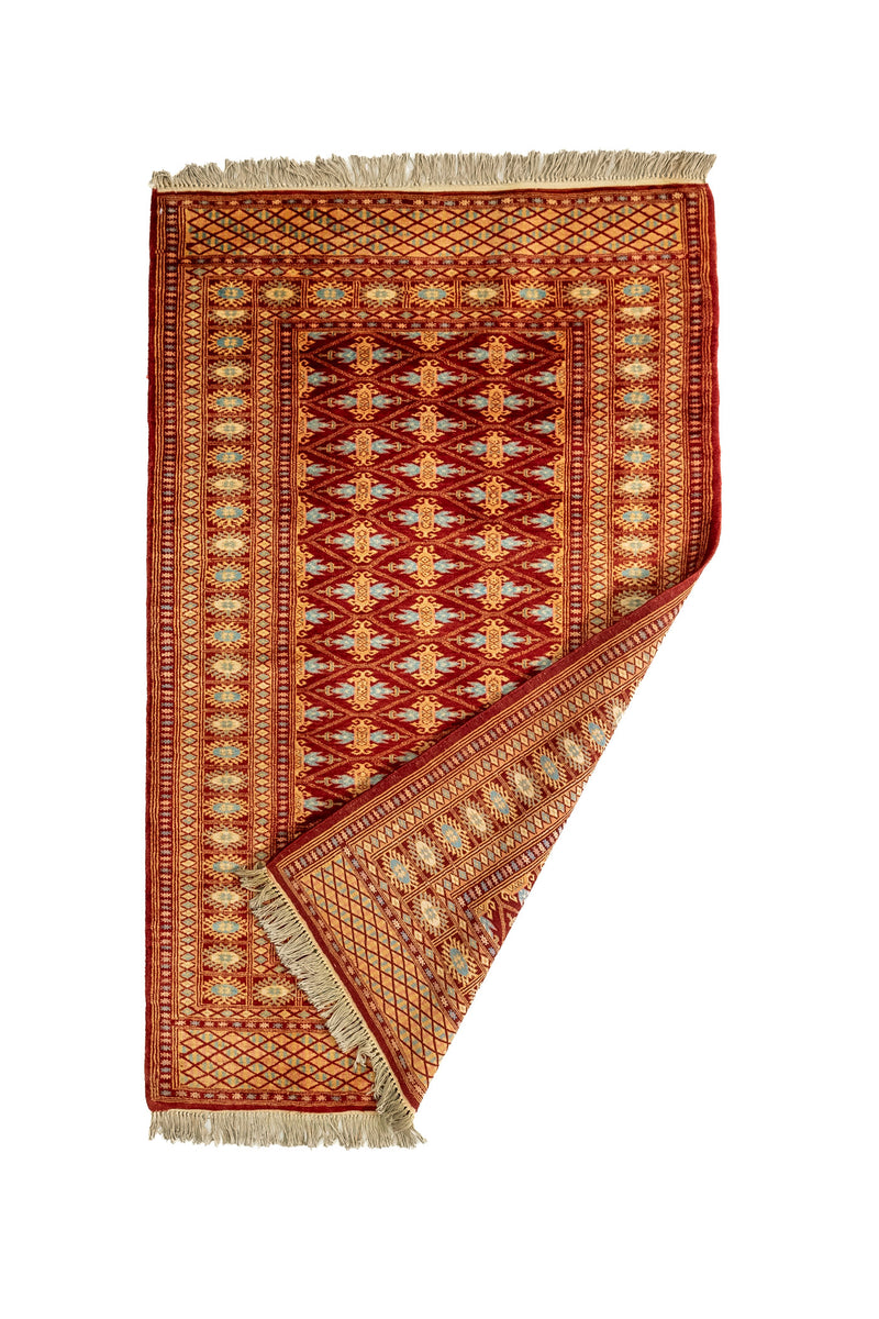 Alfombra mostrada parcialmente doblada, revelando el reverso y los bordes decorativos en detalle.