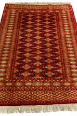 Imagen en perspectiva baja de la alfombra, resaltando el diseño central repetitivo y la combinación de tonos cálidos con celeste.