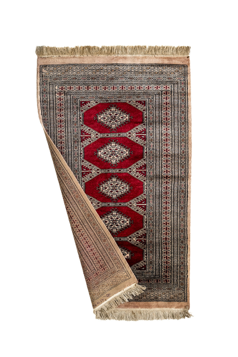 Alfombra oriental con una esquina doblada mostrando el reverso tejido y los detalles del borde y flecos.