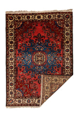 Alfombra con una esquina doblada, mostrando el reverso del tejido y el diseño central simétrico en rojo y azul.
