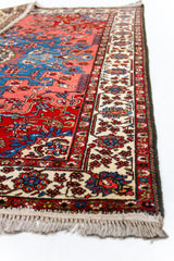 Detalle lateral de la alfombra mostrando el borde beige con flores azules y rojas, junto al campo rojo central.
