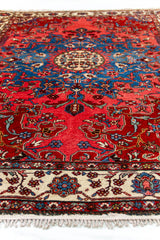 Vista en perspectiva de la alfombra con enfoque en el medallón azul central y detalles florales sobre fondo rojo.