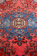 Primer plano del medallón central de la alfombra, con diseño floral simétrico en azul, beige y rojo.
