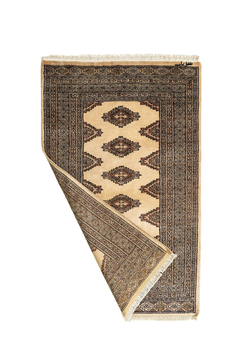 Alfombra oriental doblada mostrando el reverso, detalles de la guarda y el trabajo de tejido artesanal.