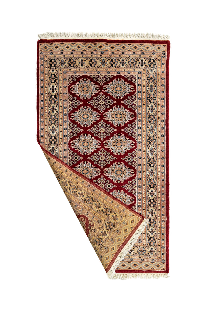 Alfombra parcialmente doblada mostrando el reverso y detalles del tejido en tonos cálidos y contrastes definidos.