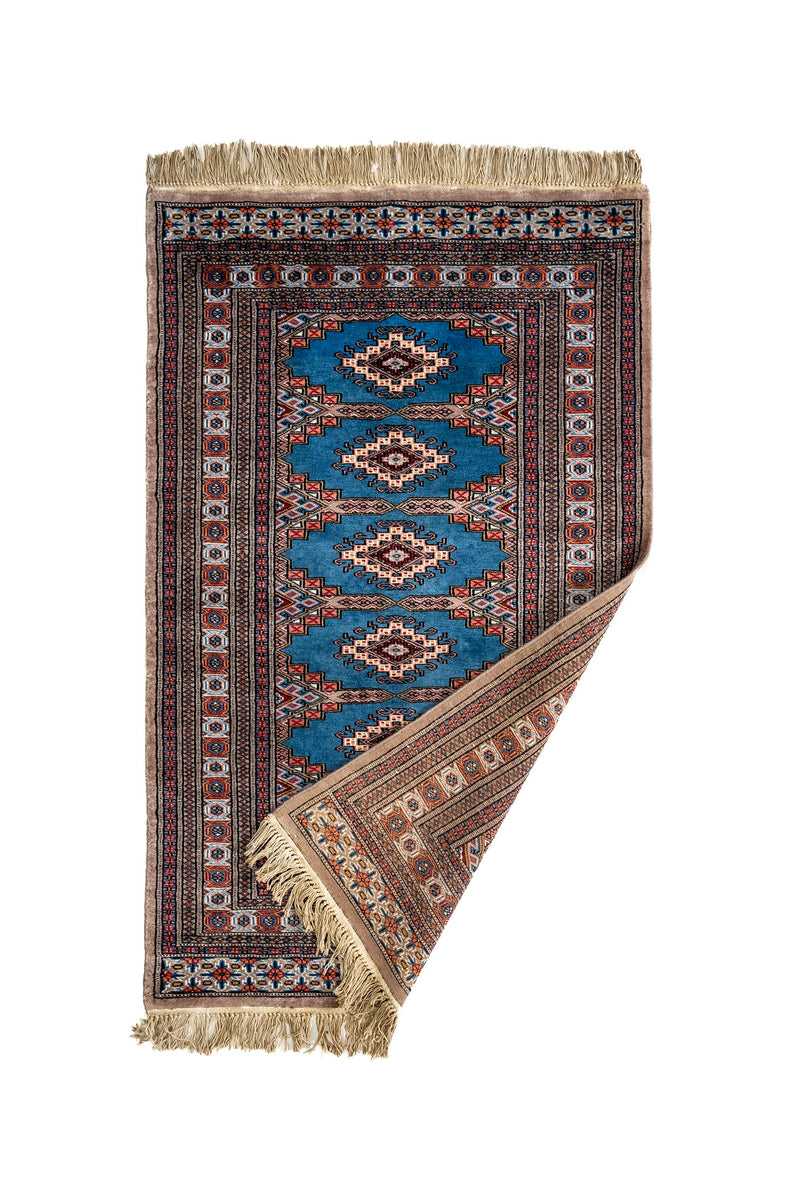 Alfombra parcialmente doblada mostrando el reverso y el borde tejido con detalles florales y geométricos.