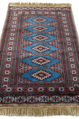 Vista en ángulo de la alfombra mostrando el diseño central repetido sobre fondo azul y el marco ornamentado.