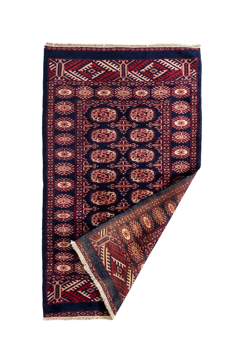 Alfombra doblada parcialmente en una esquina, mostrando el reverso del tejido con los mismos motivos tradicionales.