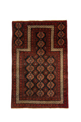 Vista frontal completa de alfombra de oración oriental con patrón geométrico en tonos rojo, negro y beige.
