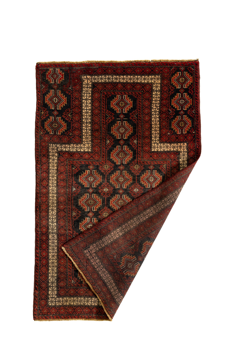 Alfombra parcialmente doblada mostrando el reverso y los bordes tejidos con motivos en rombos.