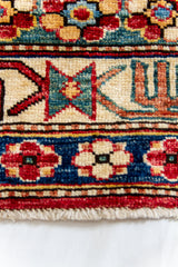 Detalle del borde inferior de la alfombra mostrando flores estilizadas sobre fondo azul y borde con flecos cortos.