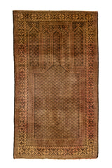 Vista superior de alfombra oriental con patrón repetitivo en tonos marrón y beige oscuro, con guarda geométrica en color rojizo.