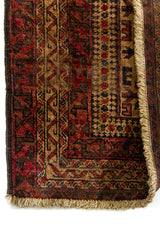Detalle del borde inferior izquierdo de la alfombra, mostrando los patrones geométricos y la calidad del tejido en tonos rojo, marrón y negro.