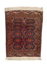 Vista superior de una alfombra oriental con fondo rojizo envejecido, detalles en azul marino y negro, y flecos marfil en ambos extremos.