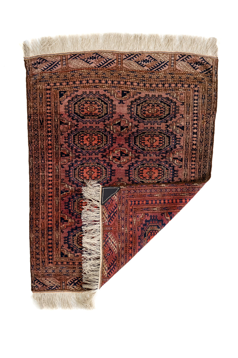 Alfombra oriental parcialmente doblada en la esquina inferior derecha, revelando el reverso del tejido y los flecos de algodón crudo.