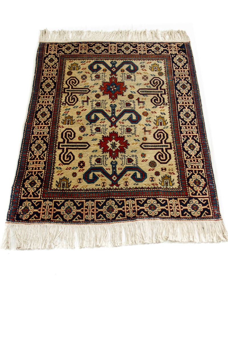 Vista en ángulo de la alfombra extendida, mostrando su estructura geométrica central y los flecos en color marfil.