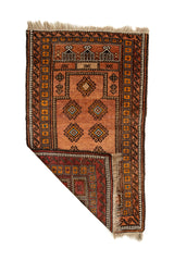 Alfombra artesanal con una esquina doblada mostrando el reverso, donde se aprecian tonos rojo oscuro, amarillo y negro con diseño de recuadros.
