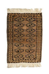 Vista completa de una alfombra oriental con fondo beige y patrón repetitivo de gul en tonos marrón oscuro y negro, acompañada de flecos marfil en ambos extremos.