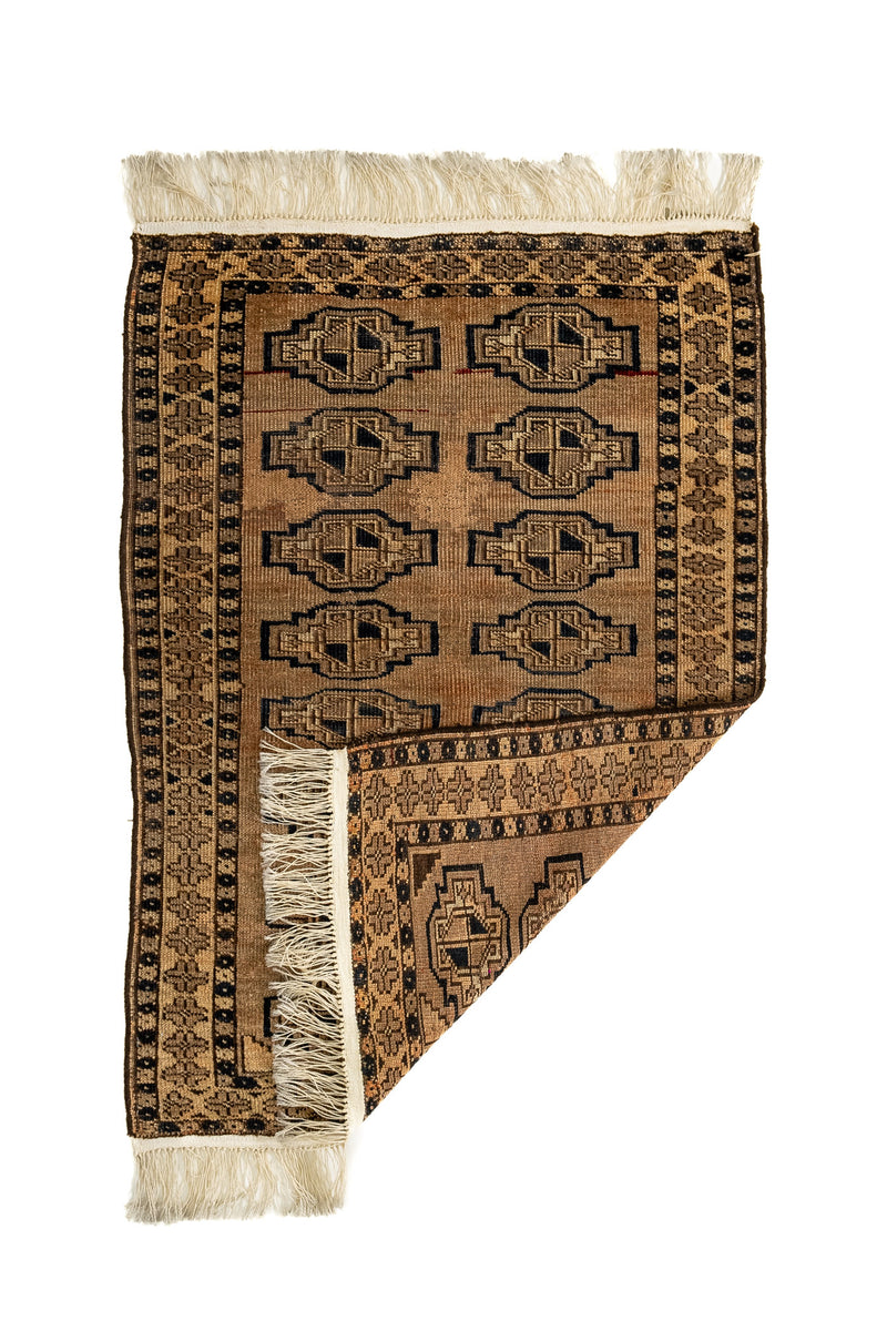 Alfombra doblada en la esquina inferior derecha, revelando el reverso del tejido y destacando el diseño geométrico y los flecos crudos.