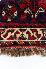 Detalle inferior de la alfombra con borde decorativo y flecos de lana marrón.