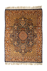 Vista superior completa de una alfombra oriental con fondo azul oscuro, detalles florales intrincados en tonos beige y terracota, y flecos en los extremos.