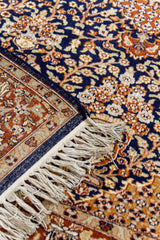 Detalle de la esquina de una alfombra oriental, destacando la textura de los flecos, el borde y el patrón floral en fondo azul profundo.