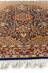 Perspectiva lateral de una alfombra oriental, mostrando el borde floral y el trabajo artesanal de los motivos en azul, terracota y crema.