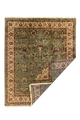 Alfombra verde con borde beige y detalles rojos, esquina doblada mostrando reverso y flecos.