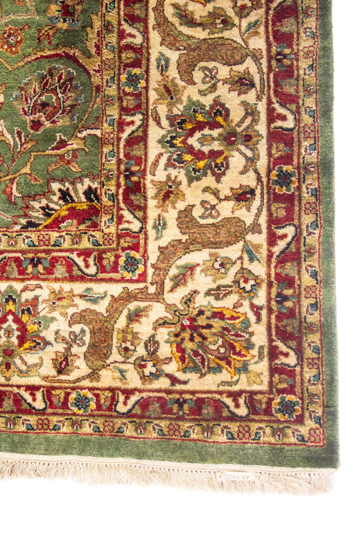 Detalle de esquina de alfombra verde oliva con guarda beige, motivos florales y flecos de algodón.
