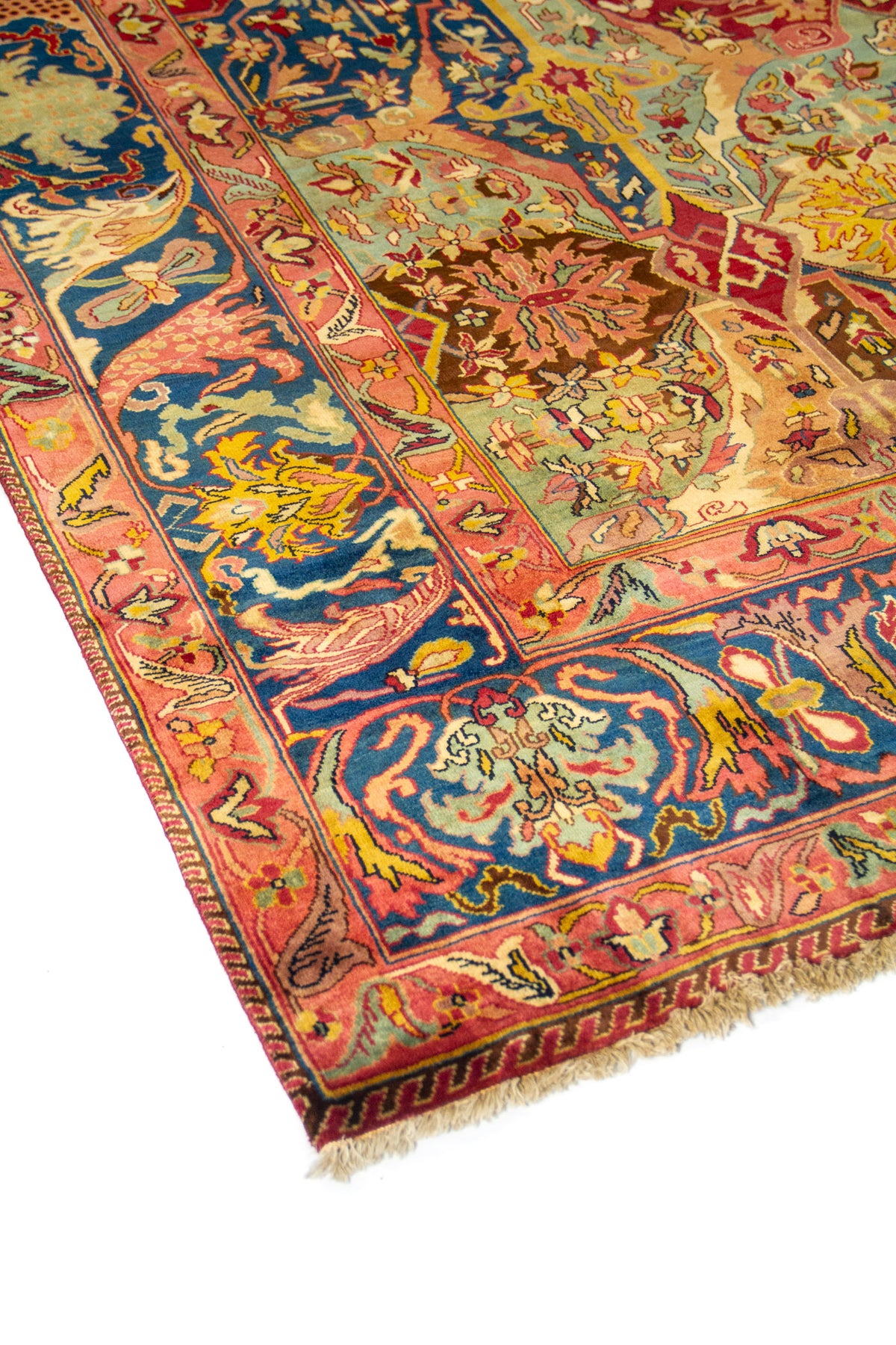 Vista en perspectiva de alfombra multicolor con campo rojo, detalles florales y amplia guarda azul decorativa.