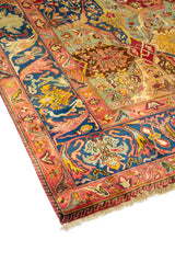 Vista en perspectiva de alfombra multicolor con campo rojo, detalles florales y amplia guarda azul decorativa.