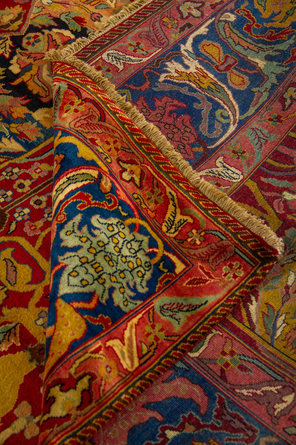 Primer plano de esquina de alfombra oriental con borde rosa, panel azul decorado y flecos claros.