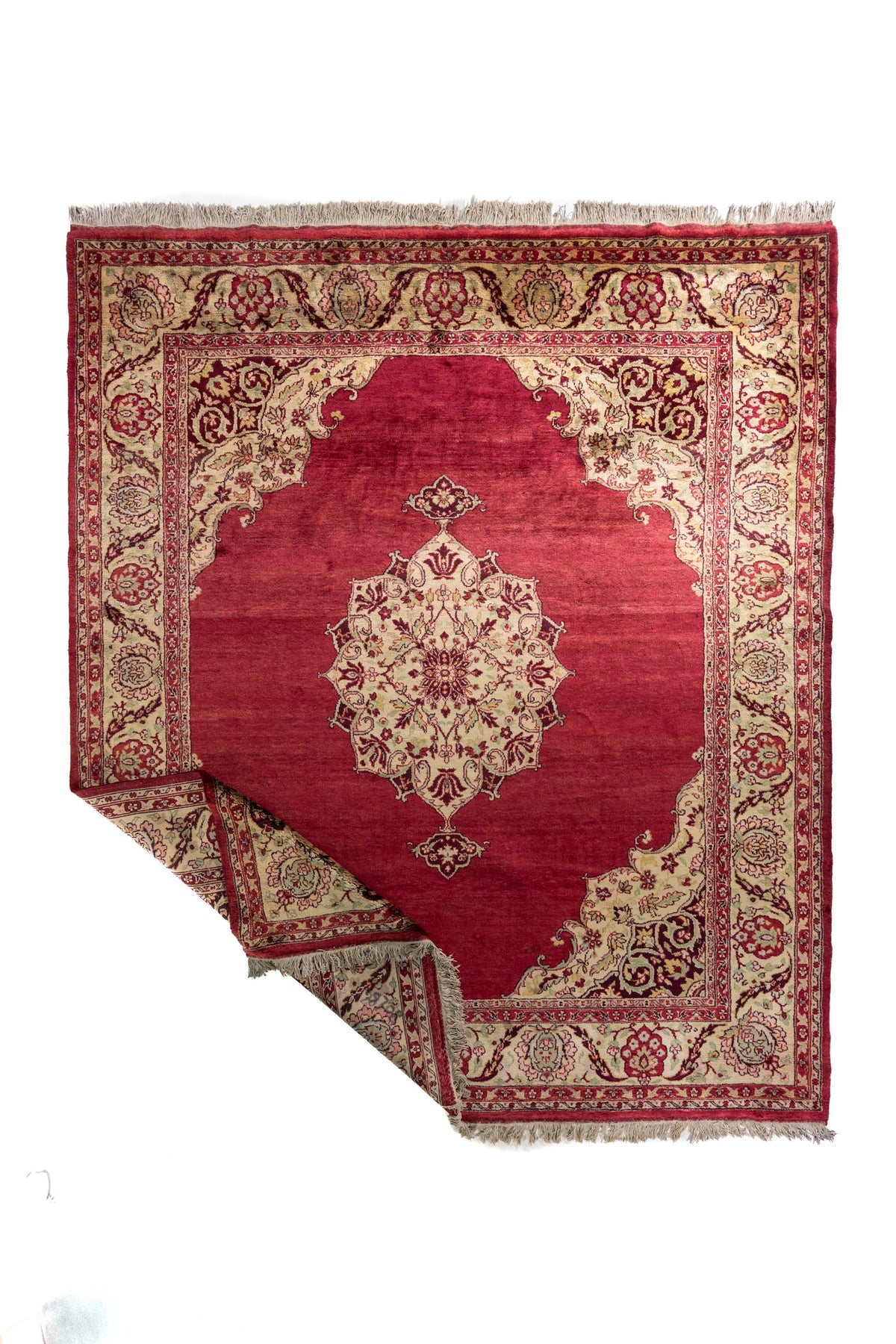 Alfombra roja burdeos con medallón central marfil y borde floral beige, esquina levantada mostrando el reverso.