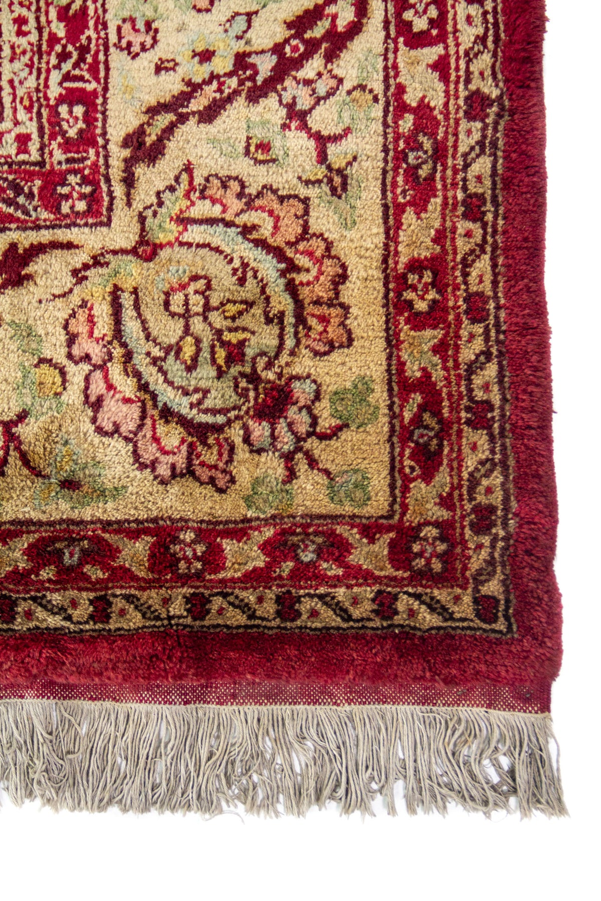 Detalle de esquina y guarda beige con motivos florales y adornos en tono rojo y verde, con flecos.