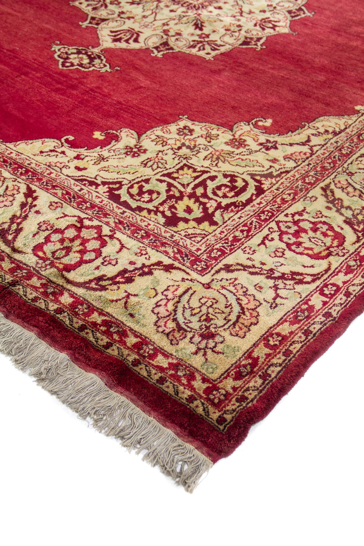 Detalle en perspectiva del borde y esquina, con patrón floral en beige, rojo y flecos claros.