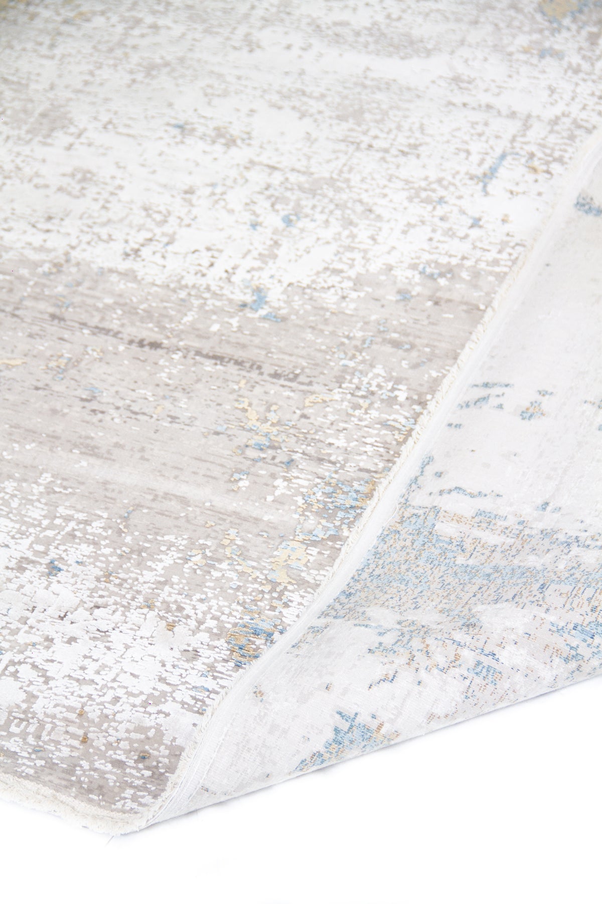 Detalle de alfombra Shadow con pliegue y reverso visible en tonos gris, blanco y celeste