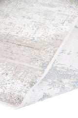 Detalle de alfombra Shadow con pliegue y reverso visible en tonos gris, blanco y celeste