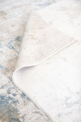 Detalle de alfombra Stradust con pliegue, reverso claro y diseño abstracto gris y celeste