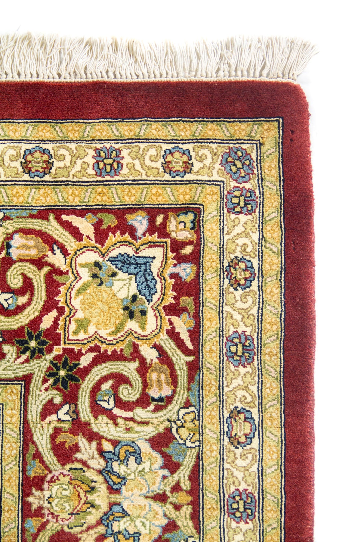 Detalle de esquina con flecos beige y guarda roja, franja beige con flores en azul y verde.