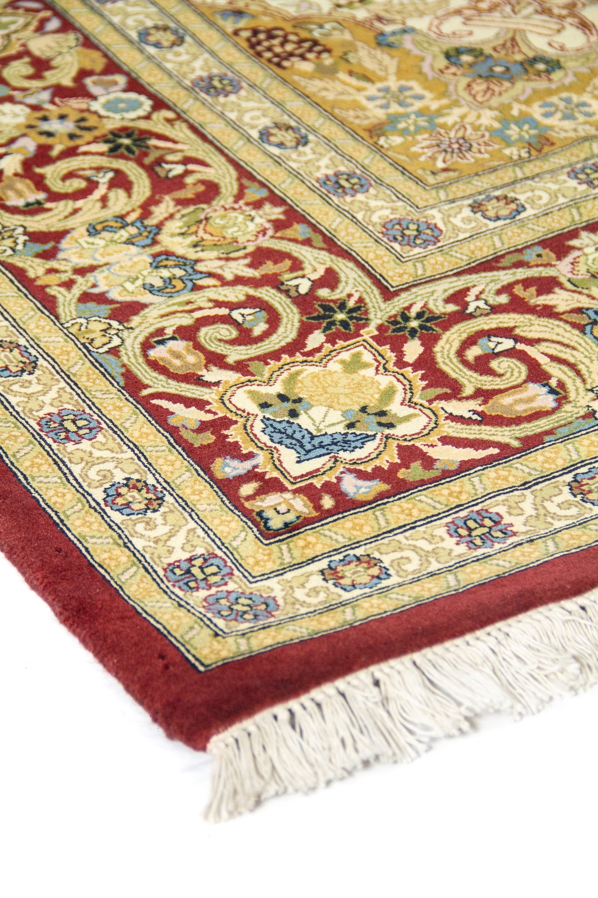 Detalle en ángulo del borde rojo y franjas beige con flores; textura del tejido y flecos visibles.