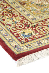 Detalle en ángulo del borde rojo y franjas beige con flores; textura del tejido y flecos visibles.