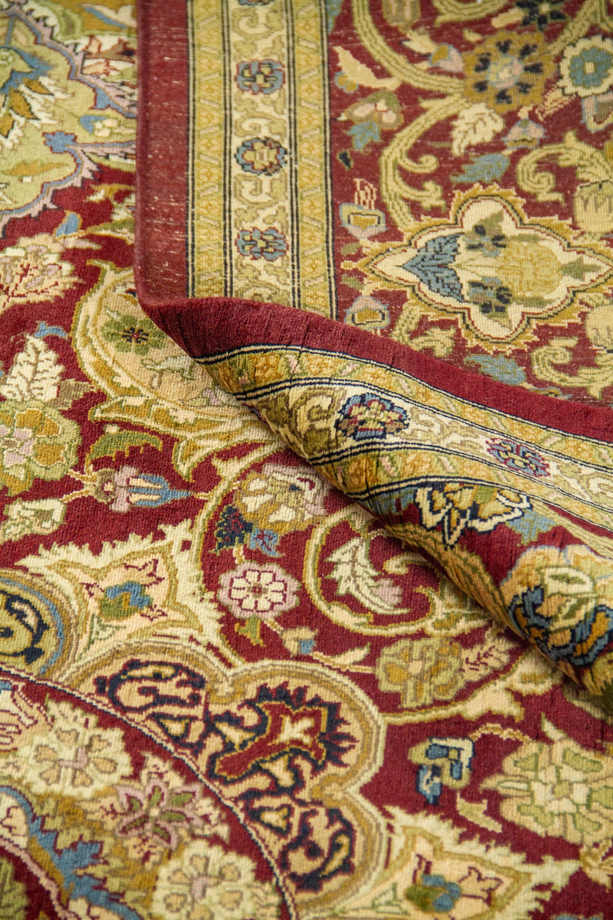 Esquina doblada de alfombra clásica mostrando el grosor y el acabado del borde rojo con diseños florales.