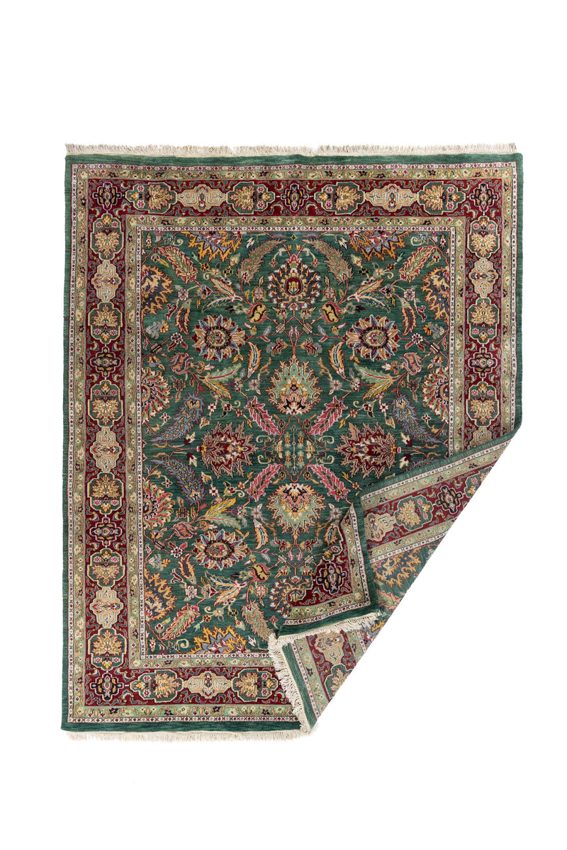 Alfombra oriental verde y rojo con esquina doblada para mostrar el reverso y el acabado del tejido.